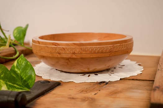 A hand-turned wooden bowl made of light pearwood with all-round decoration stands on a wooden board against a beige background