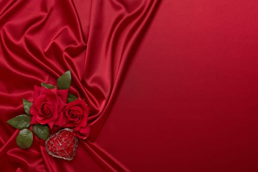 Abstract background from red silk (satin), roses and heart. Fabric texture with draped. Top view with copy space. Element design. Valentine's day. Wedding day.  Women' s day. Greeting card