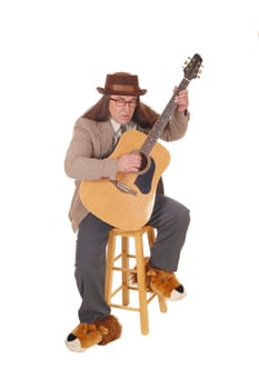 A middle age indigenous man in fancy shoes sitting and playing.his guitar in a jacket and hat, isolated for white background.