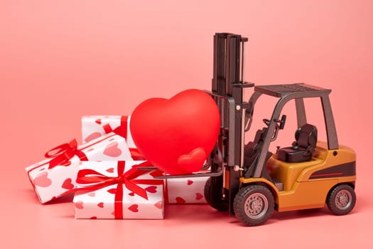Forklift, red heart and gift boxes on pink background. Valentine's Day. Wedding Day