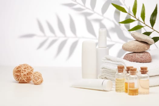 Spa still life with creams, essential oils, stones and towels on light background with shadow from plant. Healthy lifestyle, body care, Spa treatment.