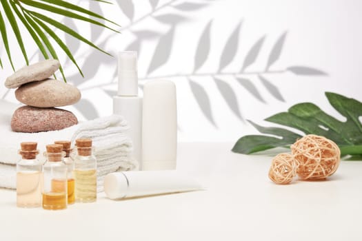 Spa still life with creams, essential oils, stones and towels on light background with shadow from plant. Healthy lifestyle, body care, Spa treatment.