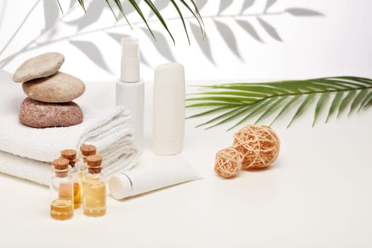 Spa still life with creams, essential oils, stones and towels on light background with shadow from plant. Healthy lifestyle, body care, Spa treatment.