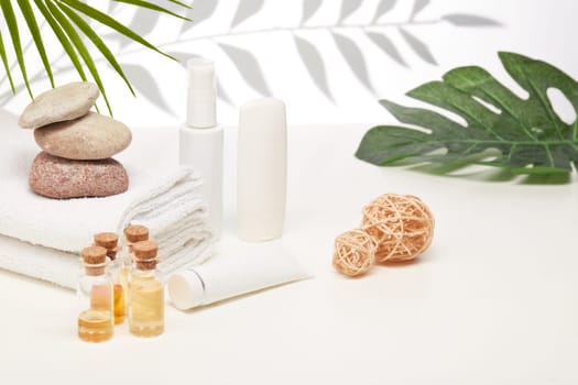 Spa still life with creams, essential oils, stones and towels on light background with shadow from plant. Healthy lifestyle, body care, Spa treatment.
