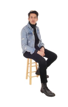 A young handsome man sitting in a jeans jacket and black pants.on a chair, resting, isolated for white background.