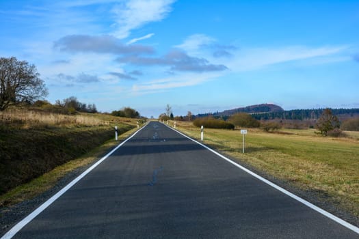 Lonely road through a green landscape, in sunlight with blue sky in the Rhoen, Bavaria, Germany
