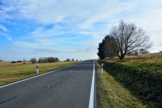 Lonely road through a green landscape, with blue sky, trees in the right side,  in the Rhoen, Bavaria, Germany