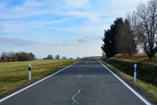 A lonely road through a green landscape, with blue sky in the Rhoen, Bavaria, Germany