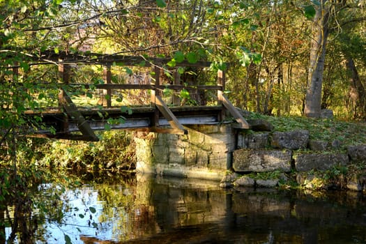 A Bridge over a stream, with many plants and an old stone wall in the golden evening light