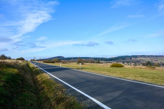 A lomg lonely road through a green landscape, with blue sky in the Rhoen, Bavaria, Germany