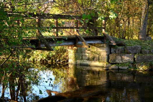 Bridge over a stream, with many plants and an old stone wall in the golden evening light