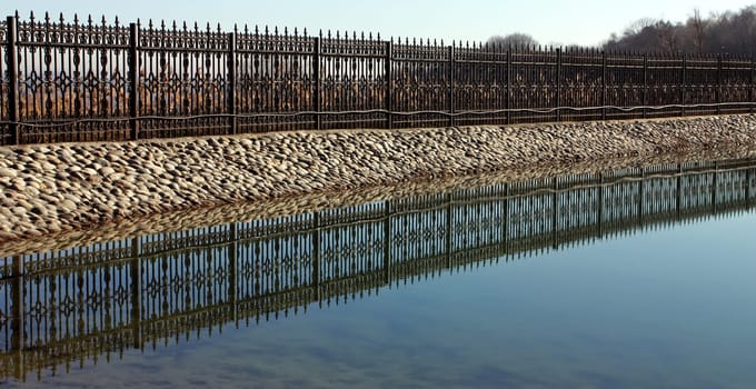 .A beautiful openwork metal fence near a decorative pond.