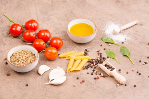 Food ingredients, italien pasta with spices like peepper corns, garlic, salt and olive oil on a brown textured stone background, empty space for text
