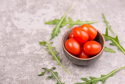 Red cherry tomatoes and fresh arugula leaves on a grey textured bakcground, empty copy space for text, healthy salad