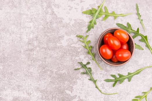 Red cherry tomatoes and fresh arugula leaves on a grey textured bakcground, empty copy space for text, healthy salad