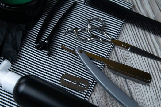 Flat lay from hairdressing accessories including: haircuts, scissors, combs, gels for styling and shaving laid out on a striped towel that stands on a wooden table. Top views