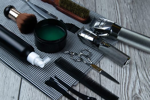 Flat lay from hairdressing accessories including: haircuts, scissors, combs, gels for styling and shaving laid out on a striped towel that stands on a wooden table. Top views