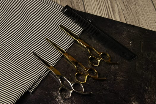 Flat lay from hairdressing accessories including: haircuts, scissors, combs, gels for styling and shaving laid out on a striped towel that stands on a wooden table. Top views