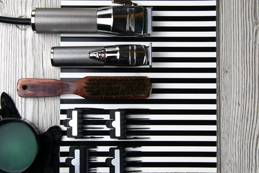 Haircut machines, nozzles of different sizes, combs and gels for styling, laid out on a beautiful black white striped background which stands on a gray wooden table. Clear space