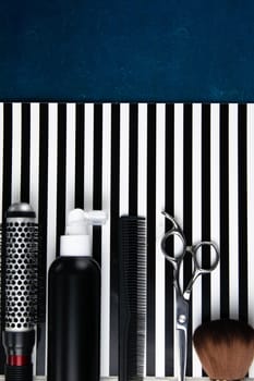 Haircut machines, nozzles of different sizes, combs and gels for styling, laid out on a beautiful black white striped background which stands on a gray wooden table. Clear space