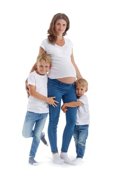 Friendly family. Two little sons are smiling and embracing pregnant mother, isolated on a white background. Happy parent. Pregnant woman and children. Concept of people and family
