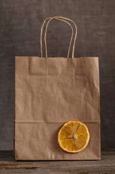 Eco-friendly paper bag on a wooden table, decorated with a slice of dry orange and a bow from a rope
