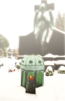 Green candle lantern on a grave on a misty graveyard