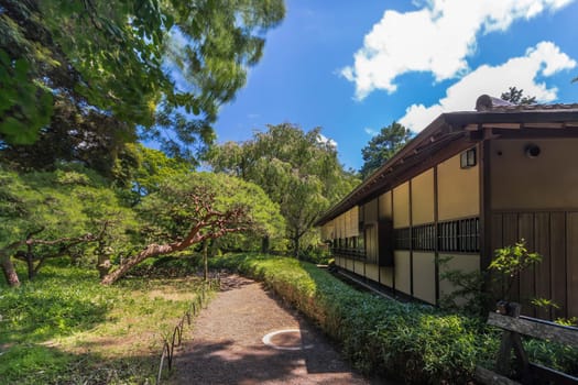 Tea House named Rakuutei lined by a path surrounded by pine trees and stone lantern in Shinjuku Gyoen Park in Tokyo in Japan.