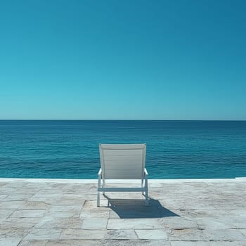 A single white lounge chair sits on a stone terrace overlooking the calm ocean. The minimalist setting and blue horizon create a peaceful and relaxing atmosphere.