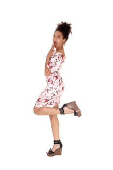 A multi-racial young woman standing in profile in a summer dress.lifting one leg up, with her curly black hair in a bun on her head, isolated.for white background.