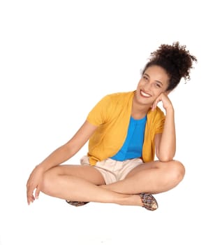 Beautiful happy multi-racial woman sitting on the floor .in shorts and a yellow sweater with her curly black hair and smiling.isolated for white background.