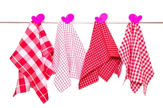 Hanging towels isolated. Closeup of various red checkered kitchen towels with violet clothespins hang on a clothes rail isolated on a white background.