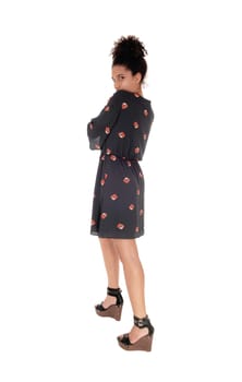 Beautiful young multi-racial woman standing in full length in a black .printed dress in profile with black hair in a bun, isolated for white .background.