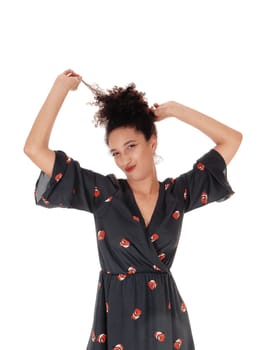 Beautiful young multi-racial woman standing in full length in a black.dress with floral print playing with her black hair in a bun on top of.her head, smiling, isolated for white background.