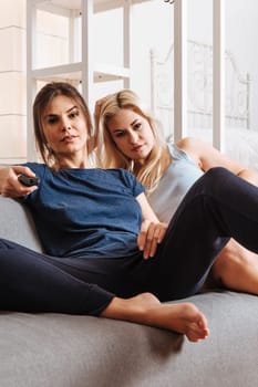 Two happy beautiful women in a relationship watching television together.