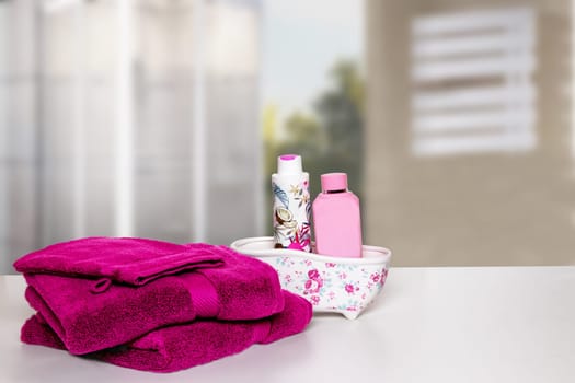 Table top on towels background. Closeup of fresh soft terry bath towels and shampoo bottles in ceramic mini bathtub on table in blurred bathroom background. Space.