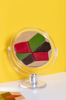 Cosmetic mirror background. Closeup of a transparent round cosmetic mirror with the magnified reflection of a wooden coaster on bright table against a yellow background. Selective focus. Macro.