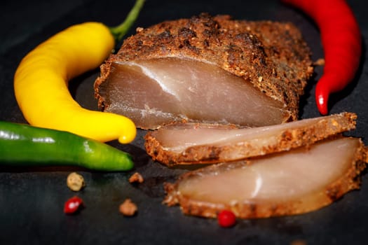 Dried chicken breast in spices, with colorful chili peppers around, against a dark background
