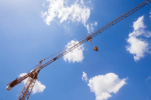 Crane for civil construction with concrete pouring bucket against blue clouds sky