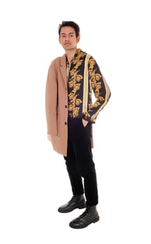 A tall skinny young man in a gold printed shirt and his hand in his.pocket, with beige coat over his shoulder, isolated for white background.