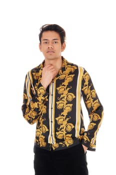 A young handsome man standing in the studio in a gold colored shirt.and black jeans, looking into the camera, isolated for white background.