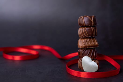Stack of Chocolate candy and red ribbon on a black background. Focus on chocolates