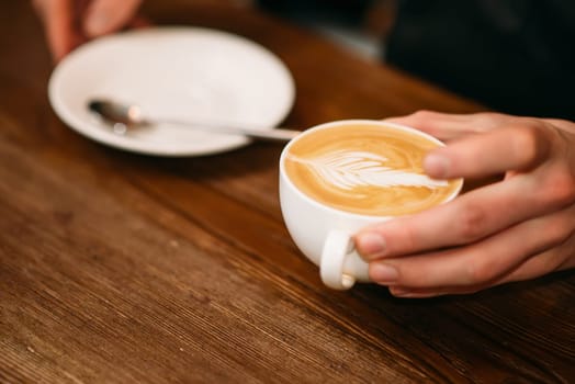 Man hands holding a cup of coffee with cream, blur background.