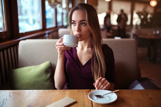 Young woman drink beverage in cafe. Beautiful girl with cup of coffee looking at the window in restaurant.