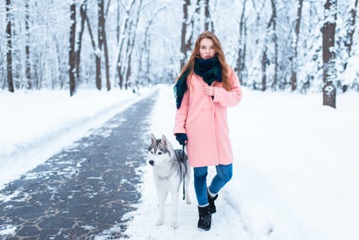 Young woman walks in the park with siberian husky, snowy forest on background. Cute girl with charming dog