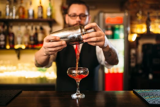 Barman is making alcohol cocktail at bar counter. Barman with shaker and glass of beverage