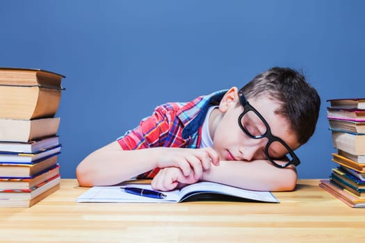 Cute child asleep at the desk in school library. Pupil in glasses against many books