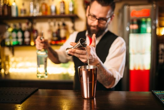 Bartender pouring alcohol beverage in metal glass at restaurant