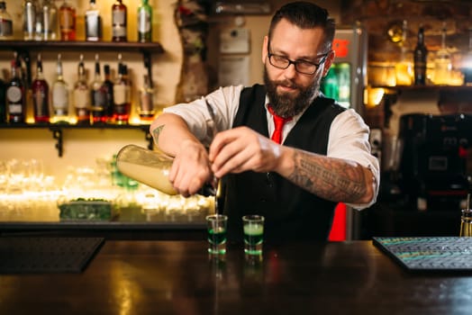 Barkeeper pouring alcoholic beverage in glass behind restaurant bar counter