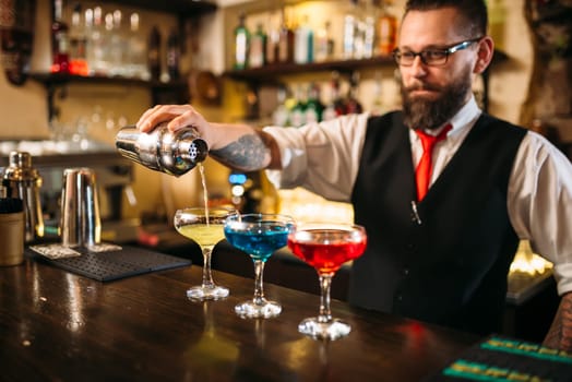 Barman with shaker making alcohol cocktails behind a bar counter in nightclub